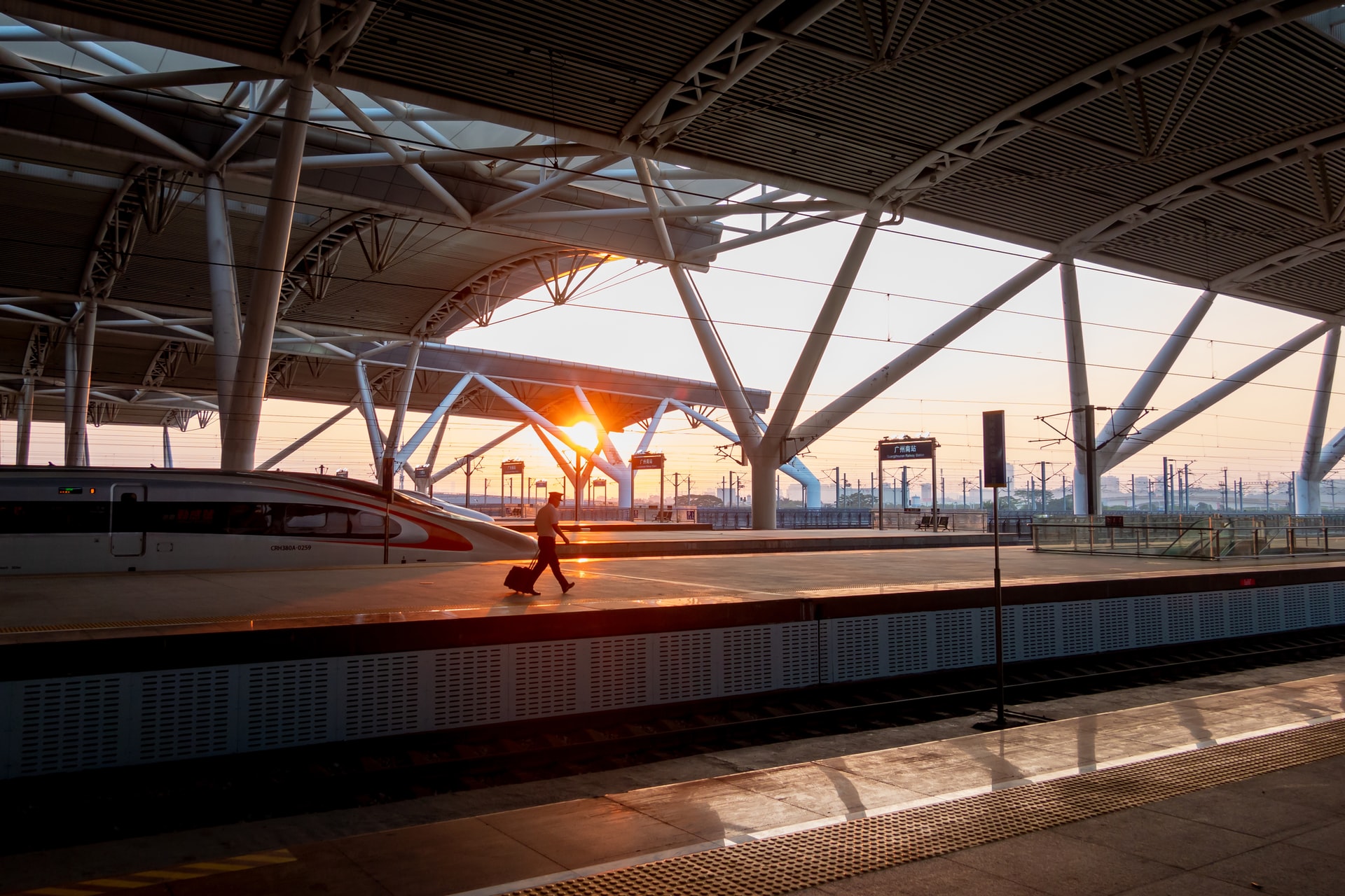 View of the sunset from a track in the station, a person walks past with a suitcase in tow