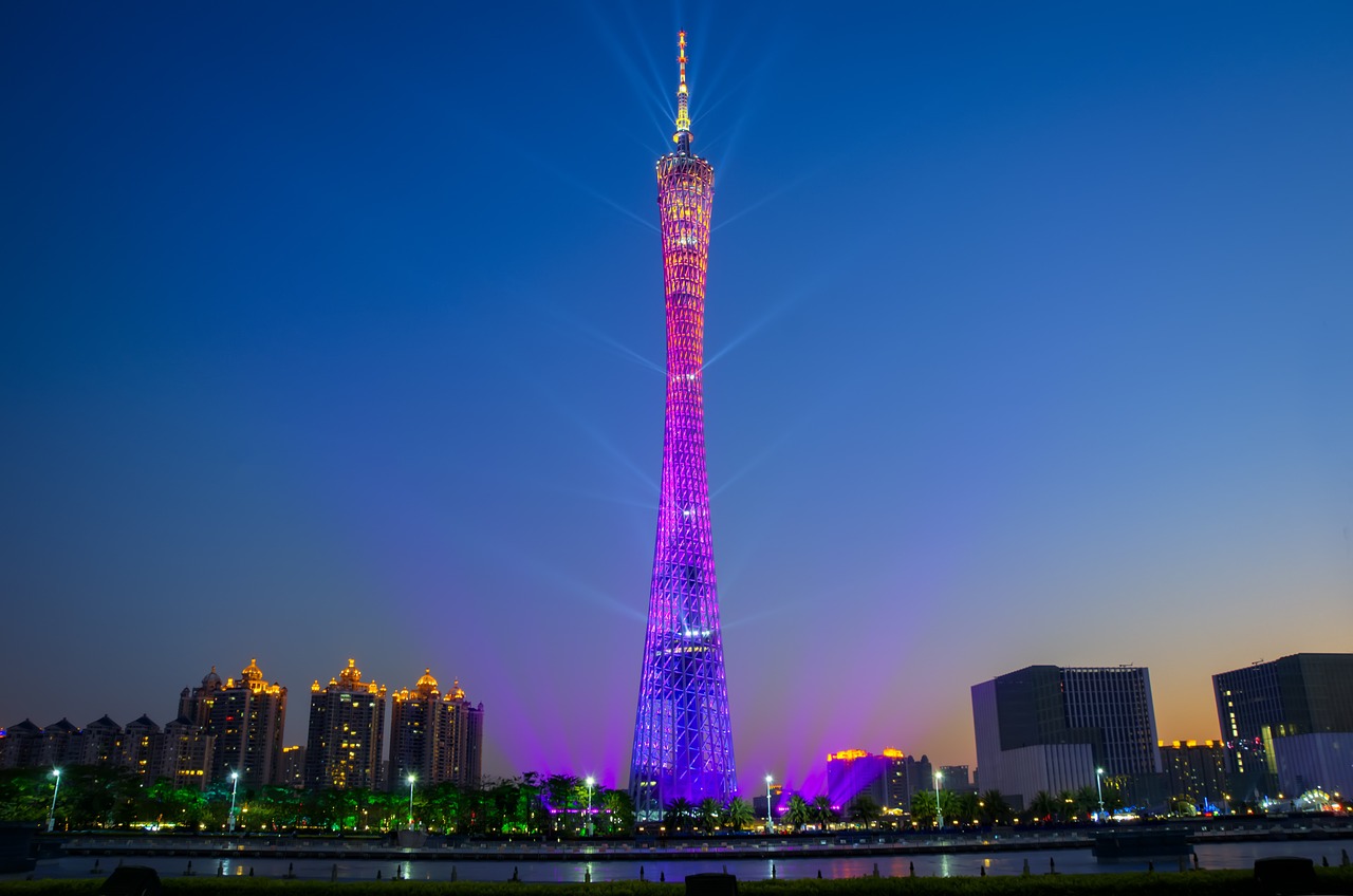 Blue-purple-pink illuminated tower that towers far above all the buildings around it and stretches far upwards