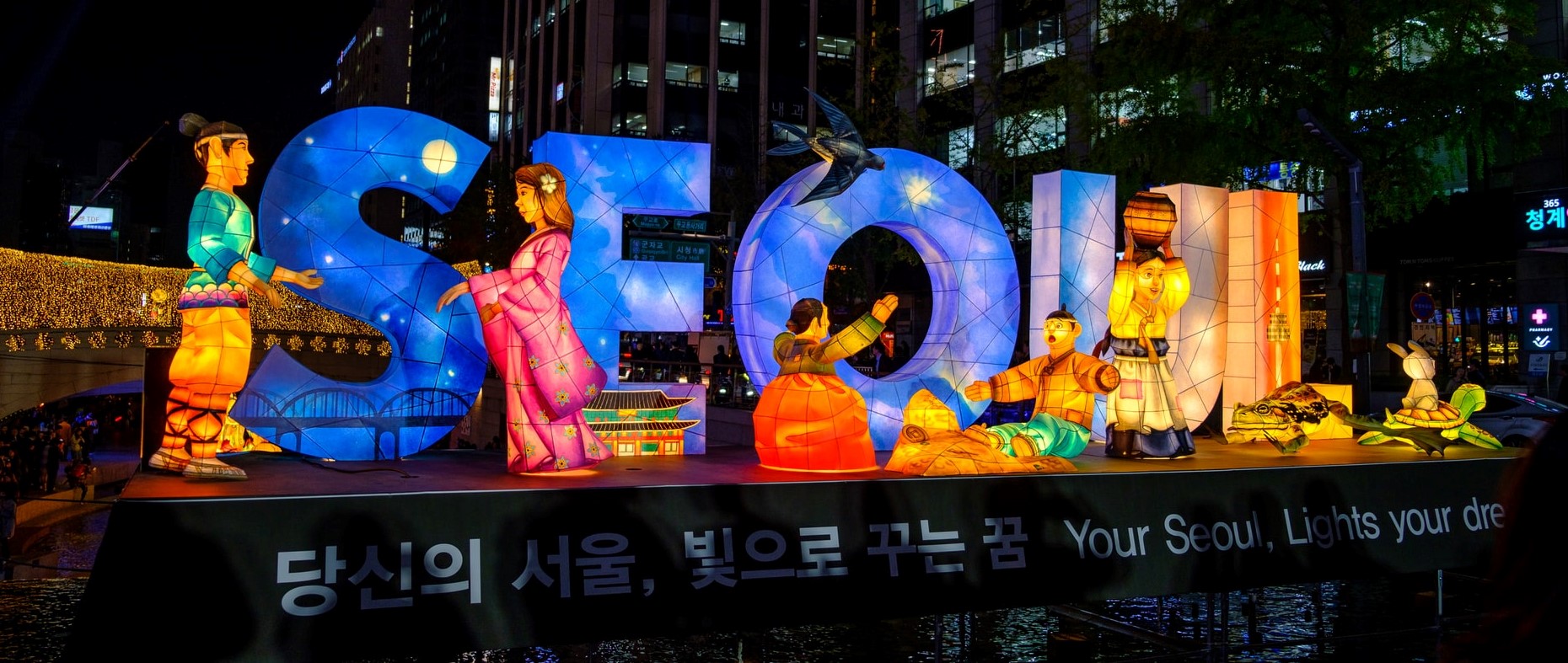 gelb und blau beleuchtete Buchstaben SEOUL umgeben von Figuren, bei Nacht