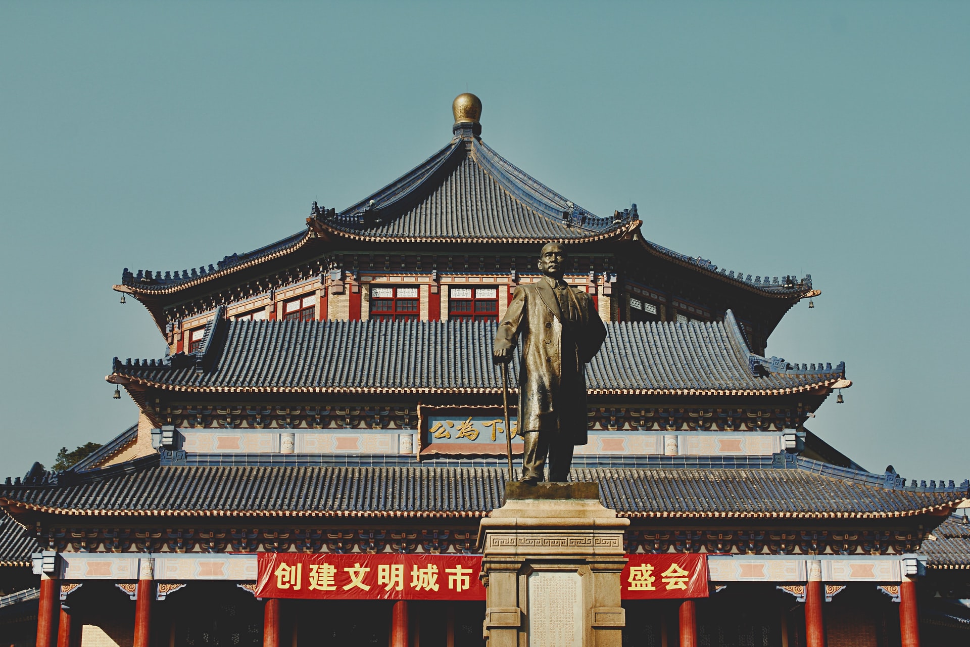 Three-storey roof of a Chinese palace with standing statue in the foreground